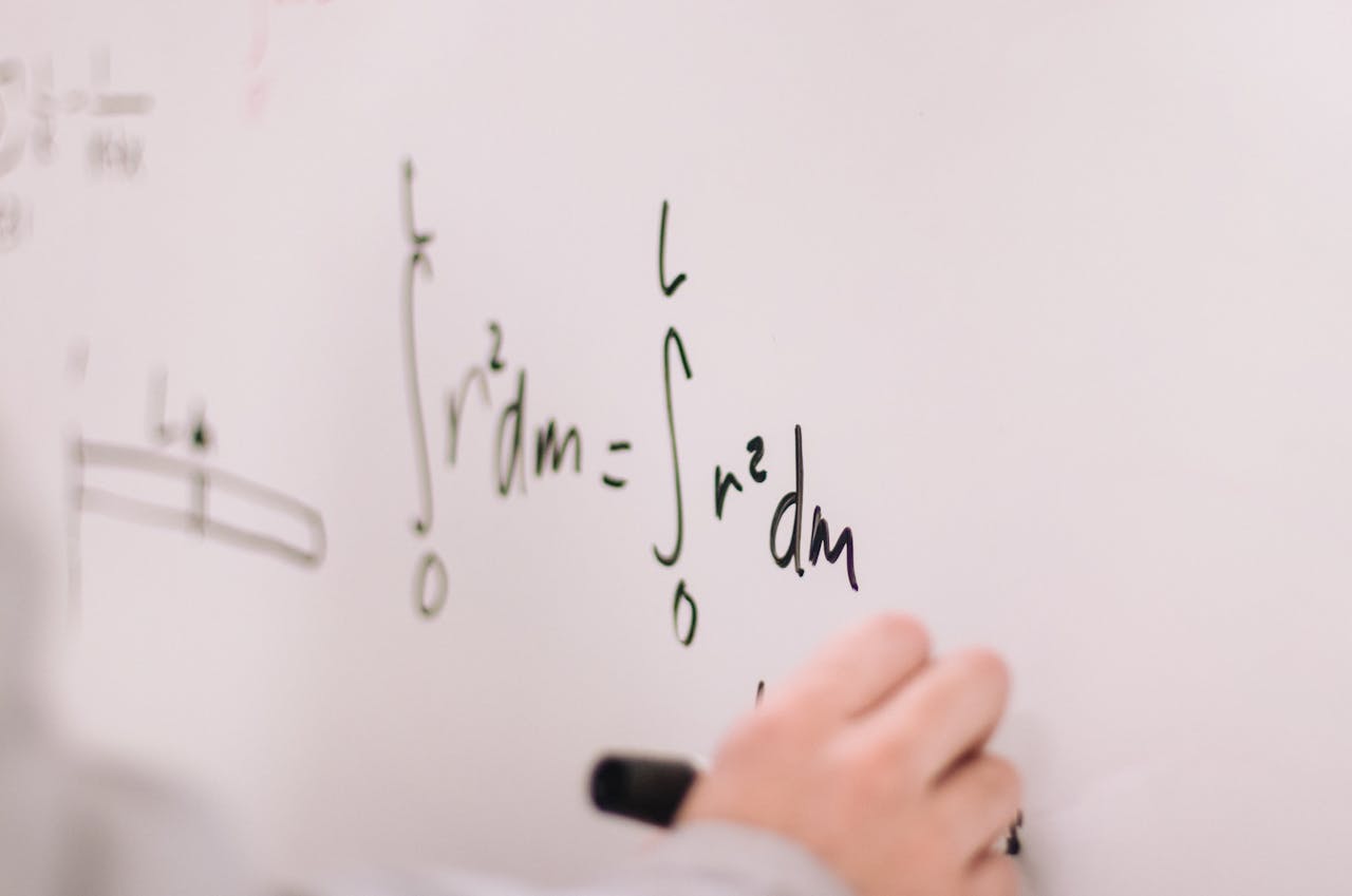 Person writing math equations on a whiteboard, focusing on integrals and formulas.